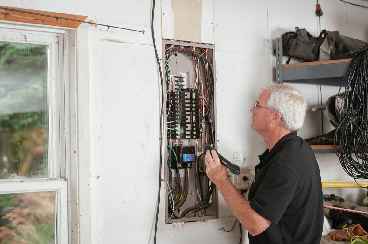 Electrician feeding copper wire through gray PVC conduit toward a residential electrical panel